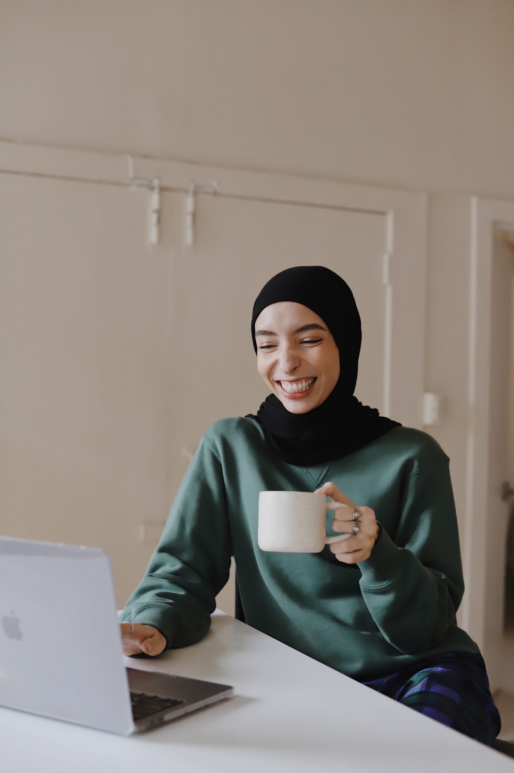 Mujer trabajando con portátil mientras sonríe y mantiene un café